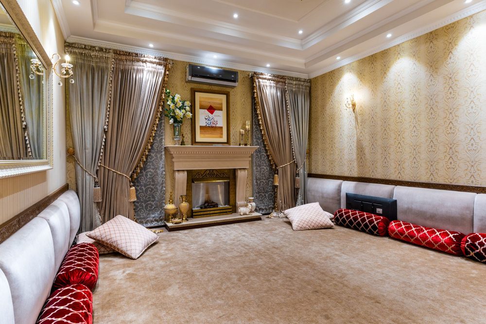 Formal living room with gold damask wallpaper panels, a fireplace flanked by tall drapes and long upholstered sofas with red cushions