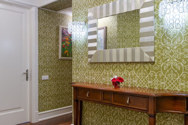 Hallway with olive-green damask wallpaper, a wooden console table and a large silver-framed mirror