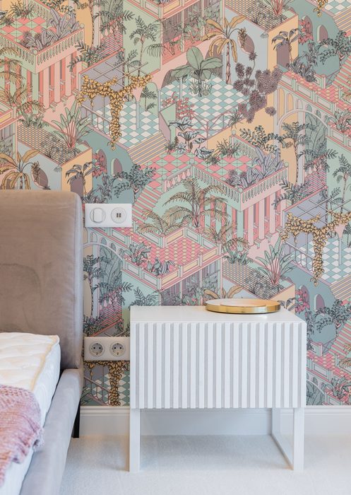 Pastel pink and green architectural-print wallpaper behind a white fluted nightstand and upholstered bed